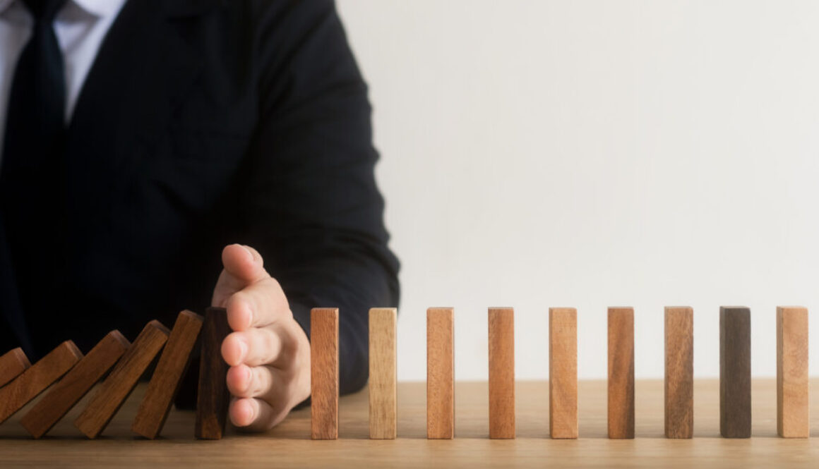 Risk management, business man hand Stop the continuous falling of wooden dominoes, stop the impact of the business crisis. hedging Solving business problems for success.